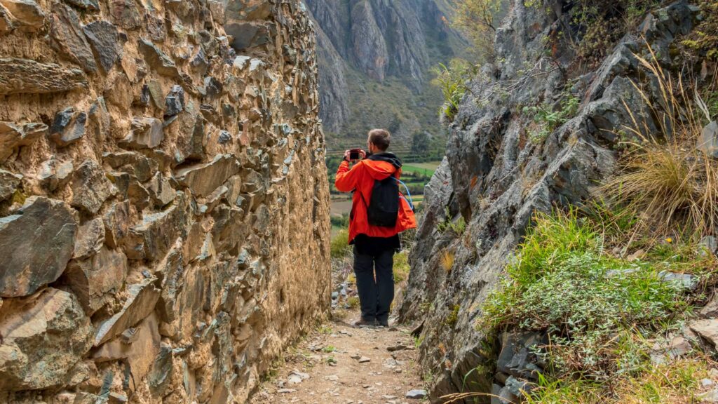 A traveler wearing a red jacket explores the ancient stone pathways of Ollantaytambo, capturing breathtaking views of the Andean mountains and lush valley - Machupicchu Andean Wonder.